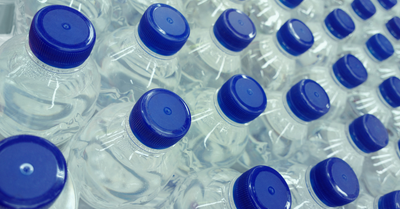 Stacked clear plastic bottles with blue screw caps ready for wholesale supply