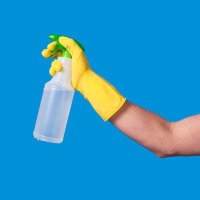 Person wearing yellow glove holding a clear plastic spray bottle for cleaning on a blue background – ideal for industrial and household use in South Africa.